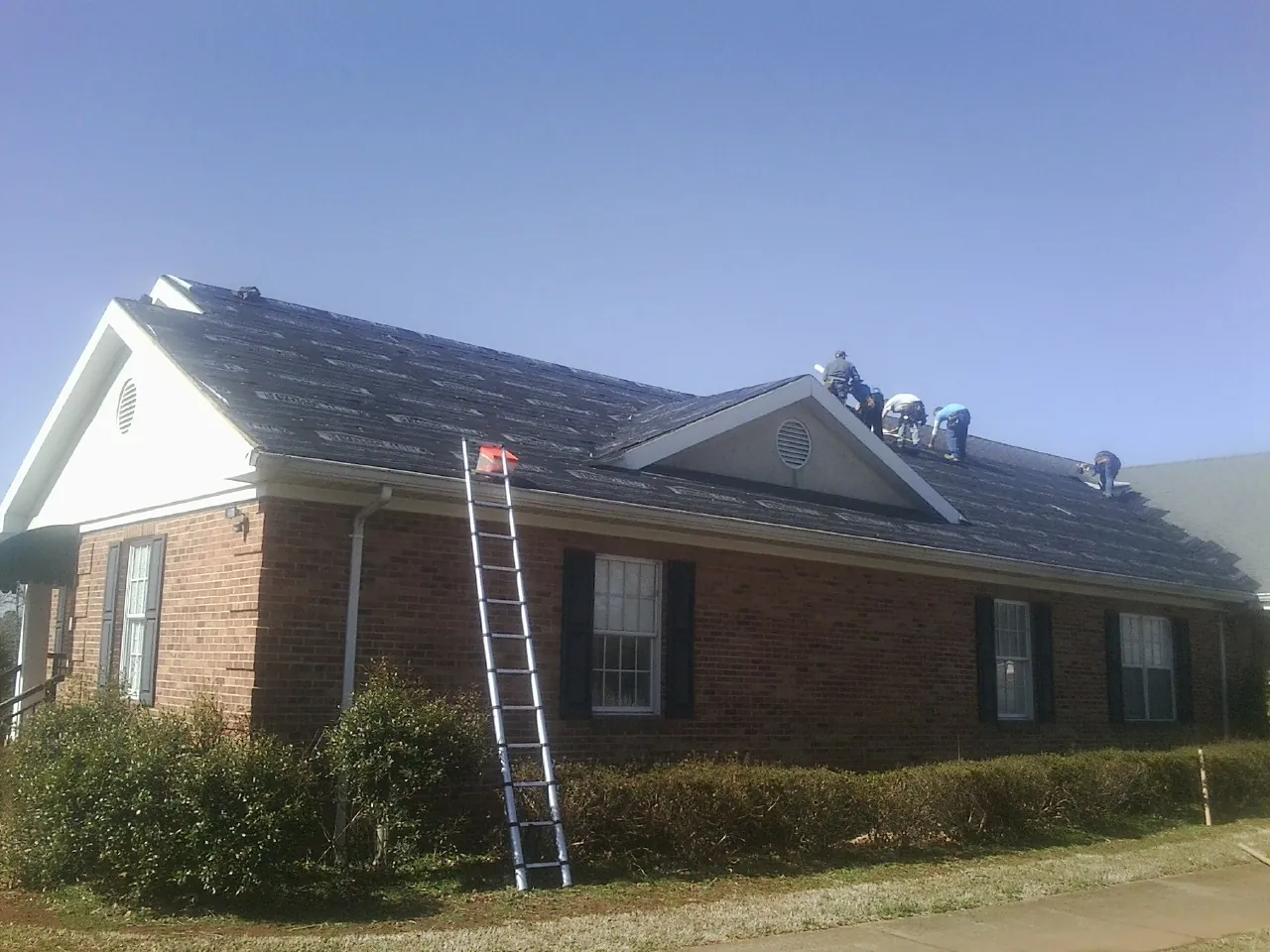 Crew tearing shingles off a brick ranch roof with a ladder set — Metal Roof Repair work by our crew in Guilderland Center