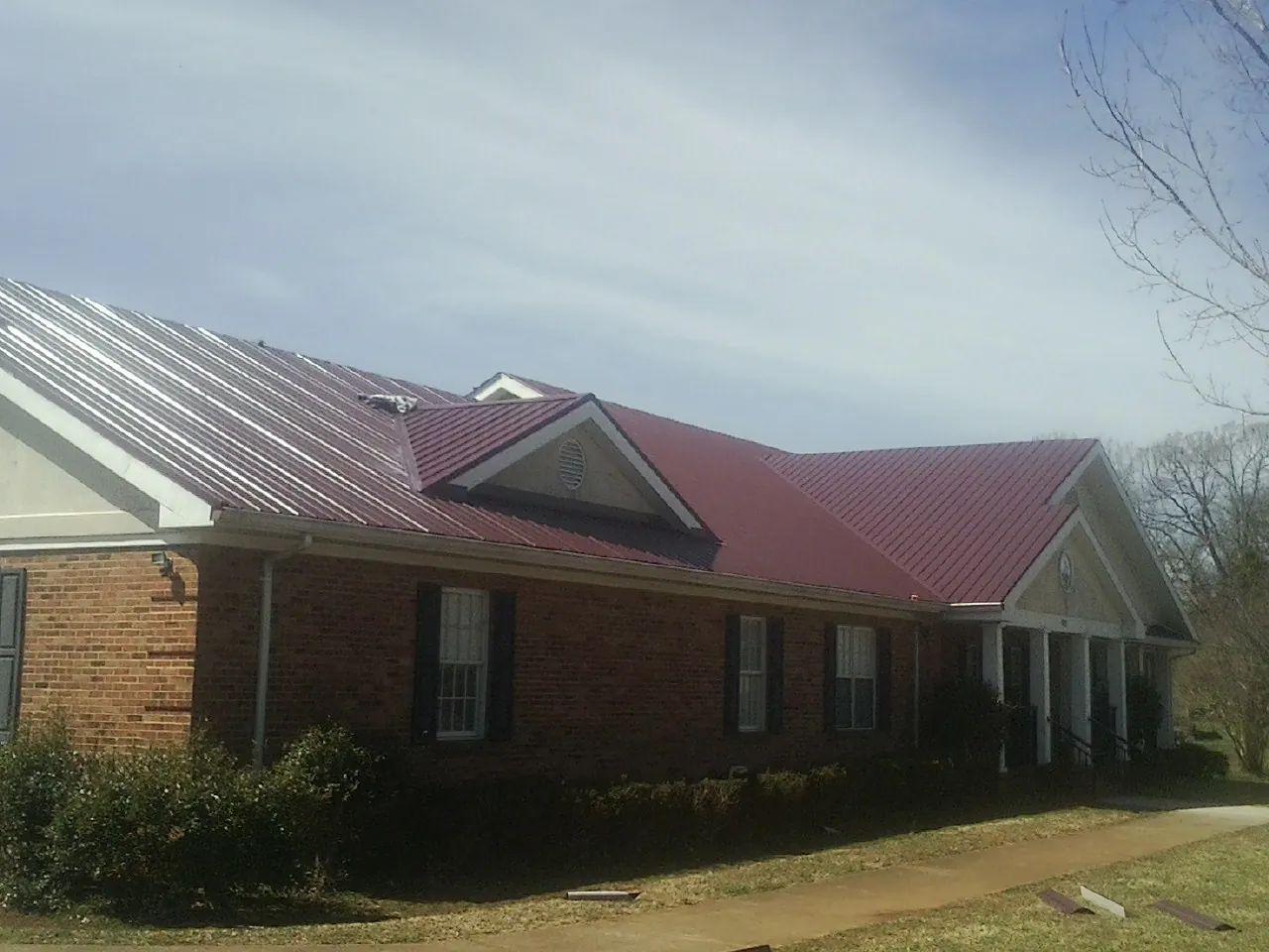 Red metal roof with gabled entries on a long brick building, from a Hail Damage Roof Repair job in Guilderland Center