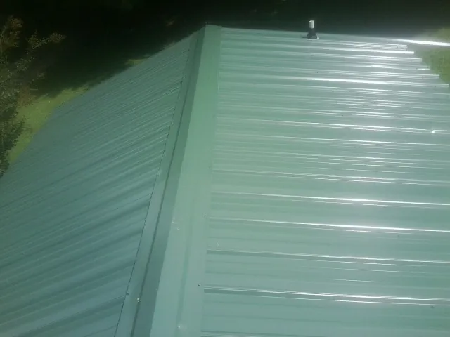 New green metal panels meeting at the ridge of a roof — Flat Roof Repair work by our crew in Guilderland Center