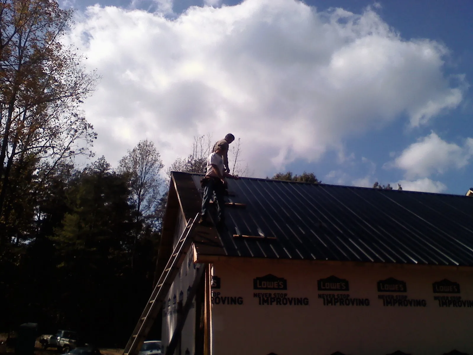 Roofer fastening dark metal panels high against a cloudy sky, from a Roof Inspection job in Guilderland Center