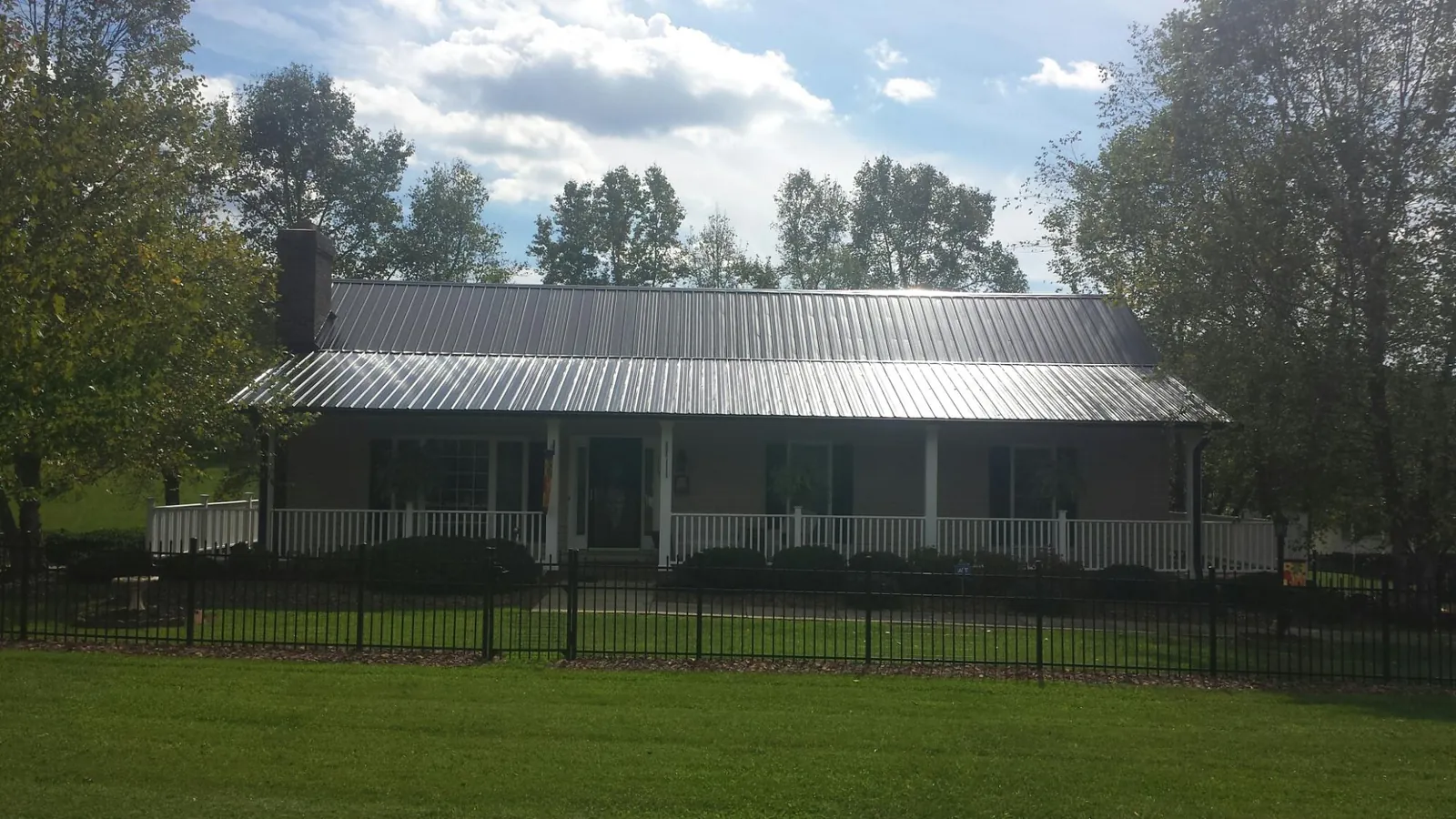 Gray metal roof on a brick ranch with a full width front porch — Gutter Guard Installation work by our crew in Guilderland Center
