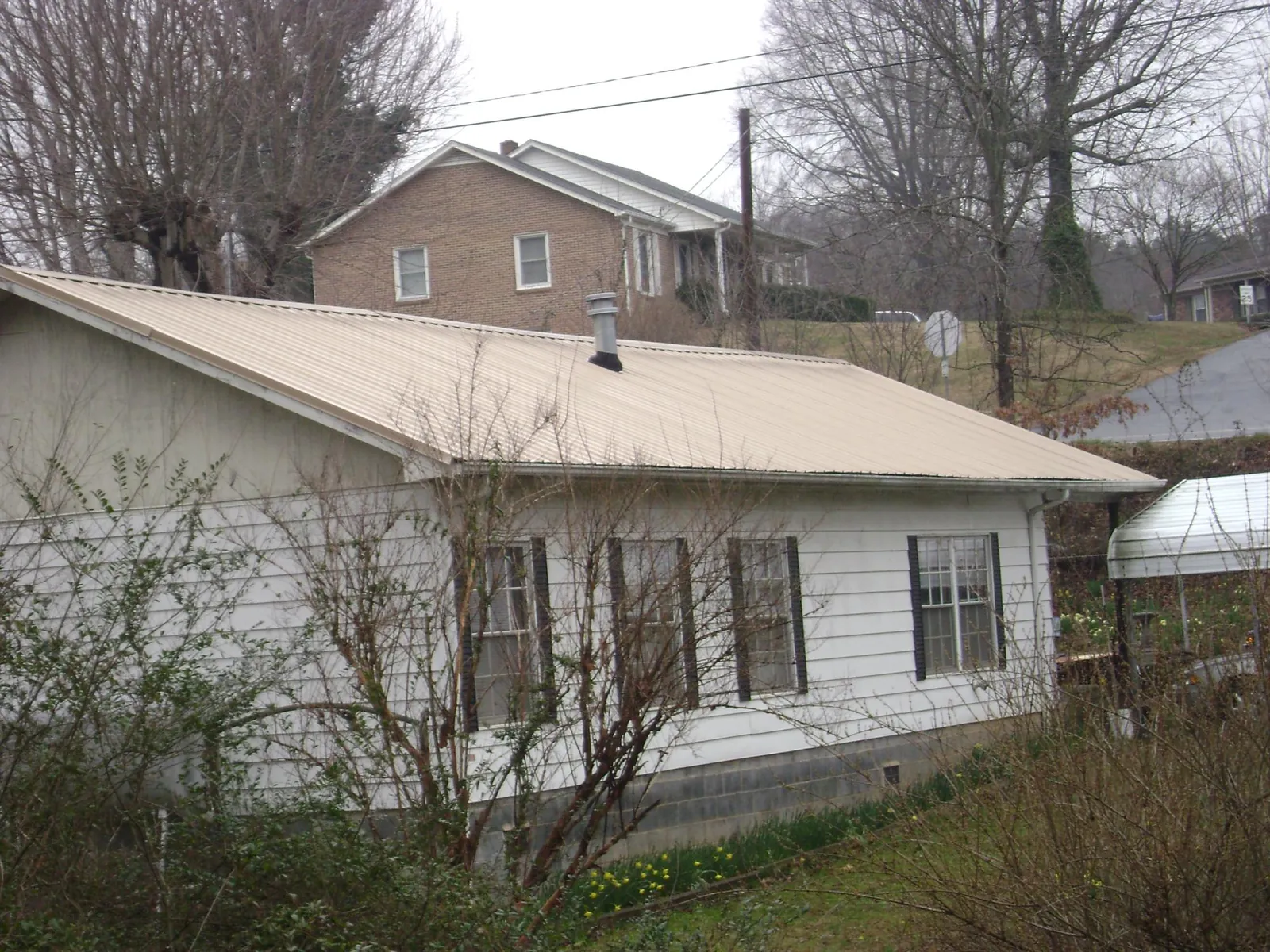 Tan metal roof on a white sided house set into a hillside — Commercial Roofing by Roofing Brothers in Guilderland Center